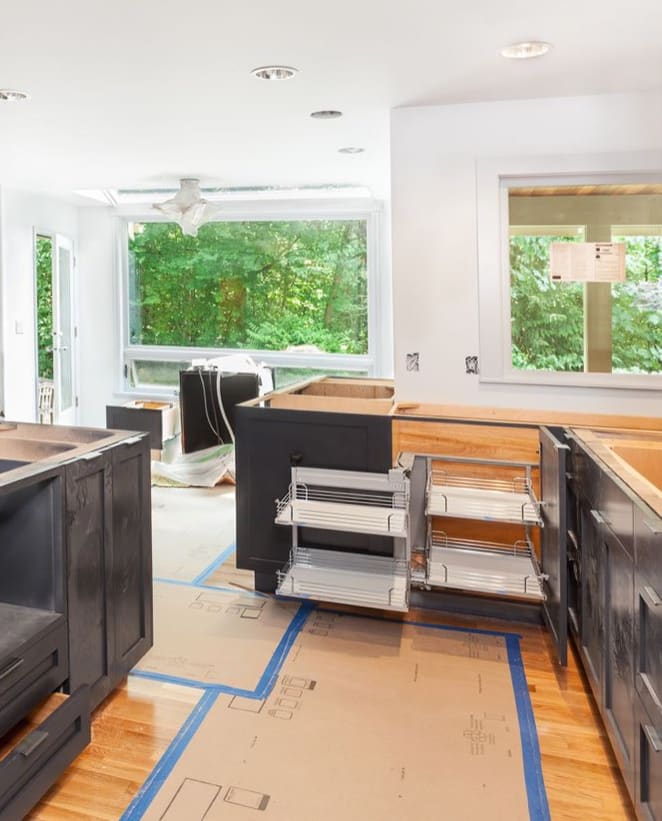 A kitchen being remodeled, with new dark cabinets and the old floor protected