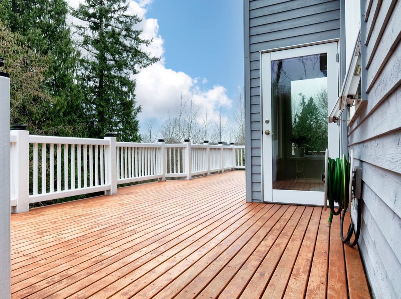 A new wooden deck with railings behind a grey house
