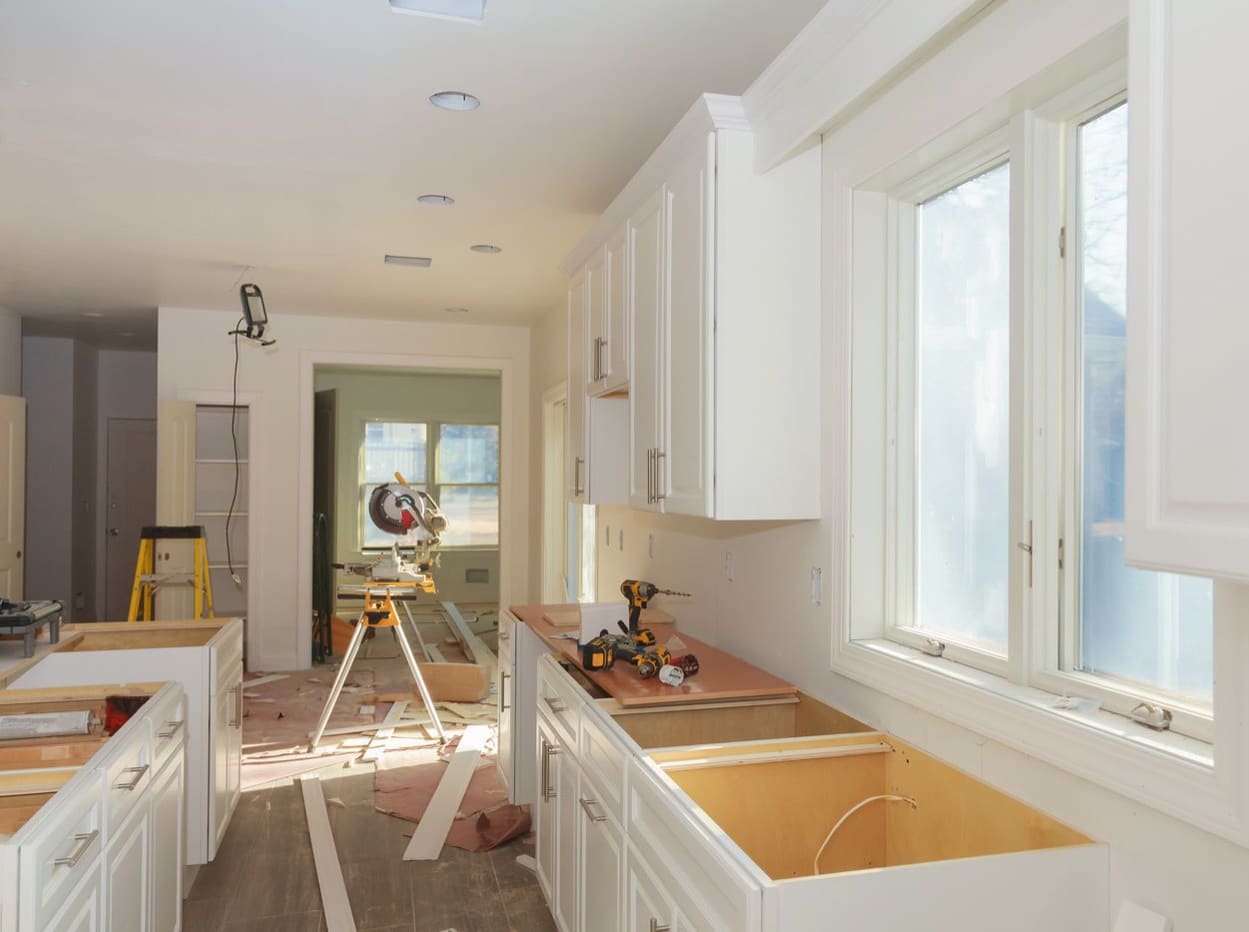 A kitchen mid-renovation with new white cabinets and a mitre saw