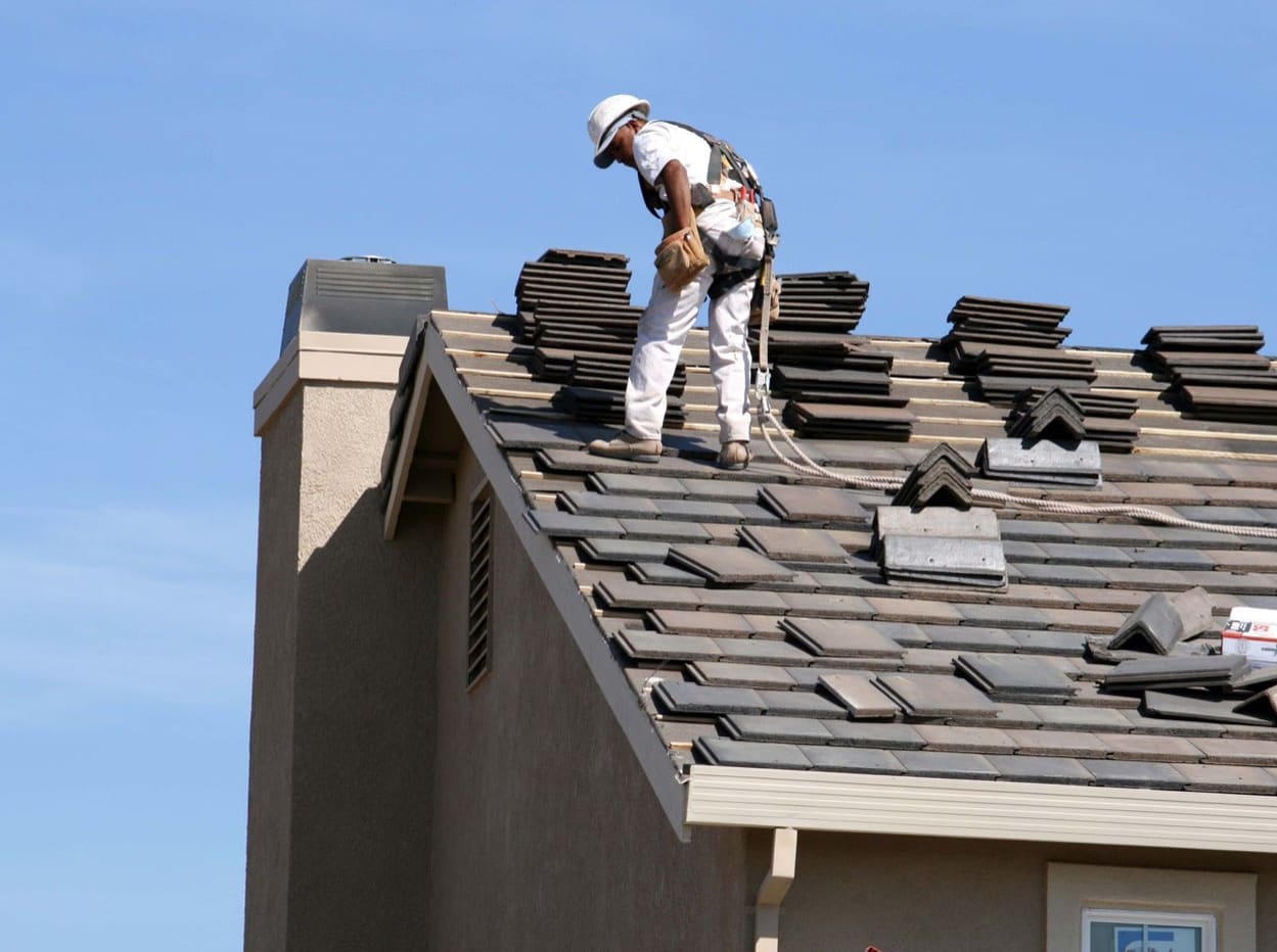 Two roofers laying underlayment on a shingle roof under a blue sky